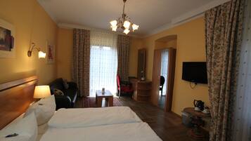 A hotel room with a large bed, a desk, a chair, a television, and a wardrobe.