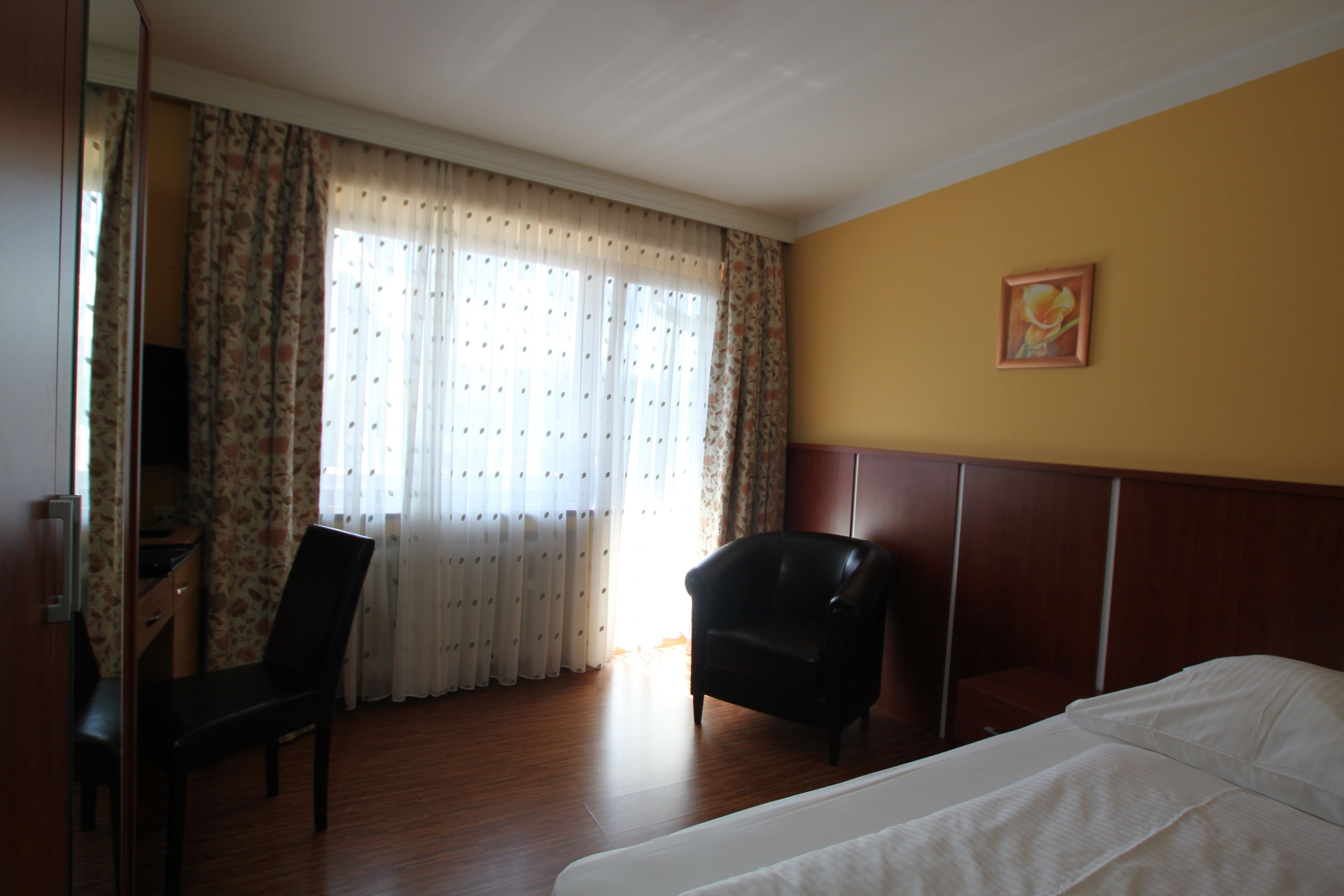 Ein Hotelzimmer mit Bett, Schreibtisch, Stuhl und einem Vorhangfenster.