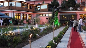 A hotel with a red carpet leading to a balcony, surrounded by a garden with stone pathways and torch lighting. - Atlas Grand Hotel (Garmisch-Partenkirchen)