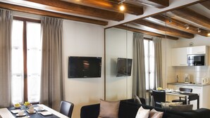 A modern living room with a black sofa, a dining table set for two, and a kitchen area with a microwave and coffee maker. - Lion d'Or Paris Hotel (Paris)