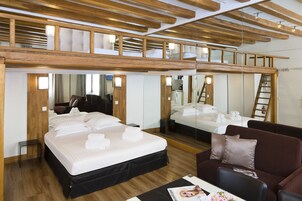 A hotel room with a loft bed, a lower bed, a sofa, and a mirror reflecting the room.