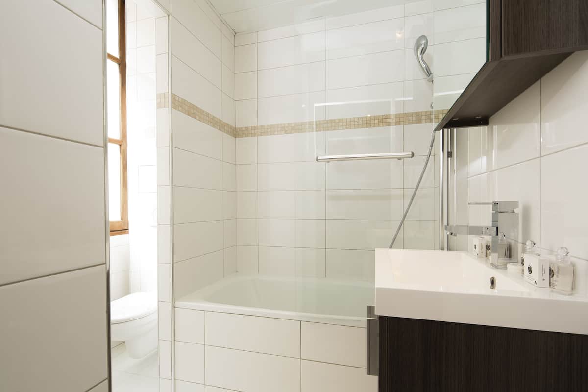Une salle de bain moderne avec des carreaux blancs, une douche à parois de verre, un lavabo blanc et un miroir au-dessus.