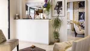 A modern hotel lobby with a reception desk, seating area, and a view of the dining area. - Lion d'Or Paris Hotel (Paris)