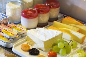 A cheese platter with various cheeses, grapes, and a small fruit.