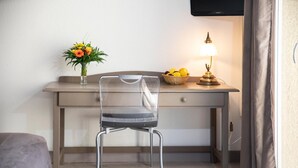 Une petite pièce moderne, équipée d’un bureau, d’une chaise, d’une lampe, d’un vase avec des fleurs et d’un panier de fruits.