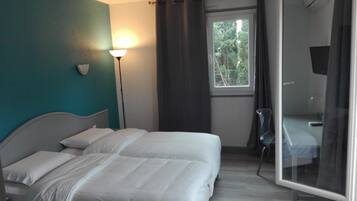 A hotel room with a bed, a bedside lamp, a window with curtains, and a chair.