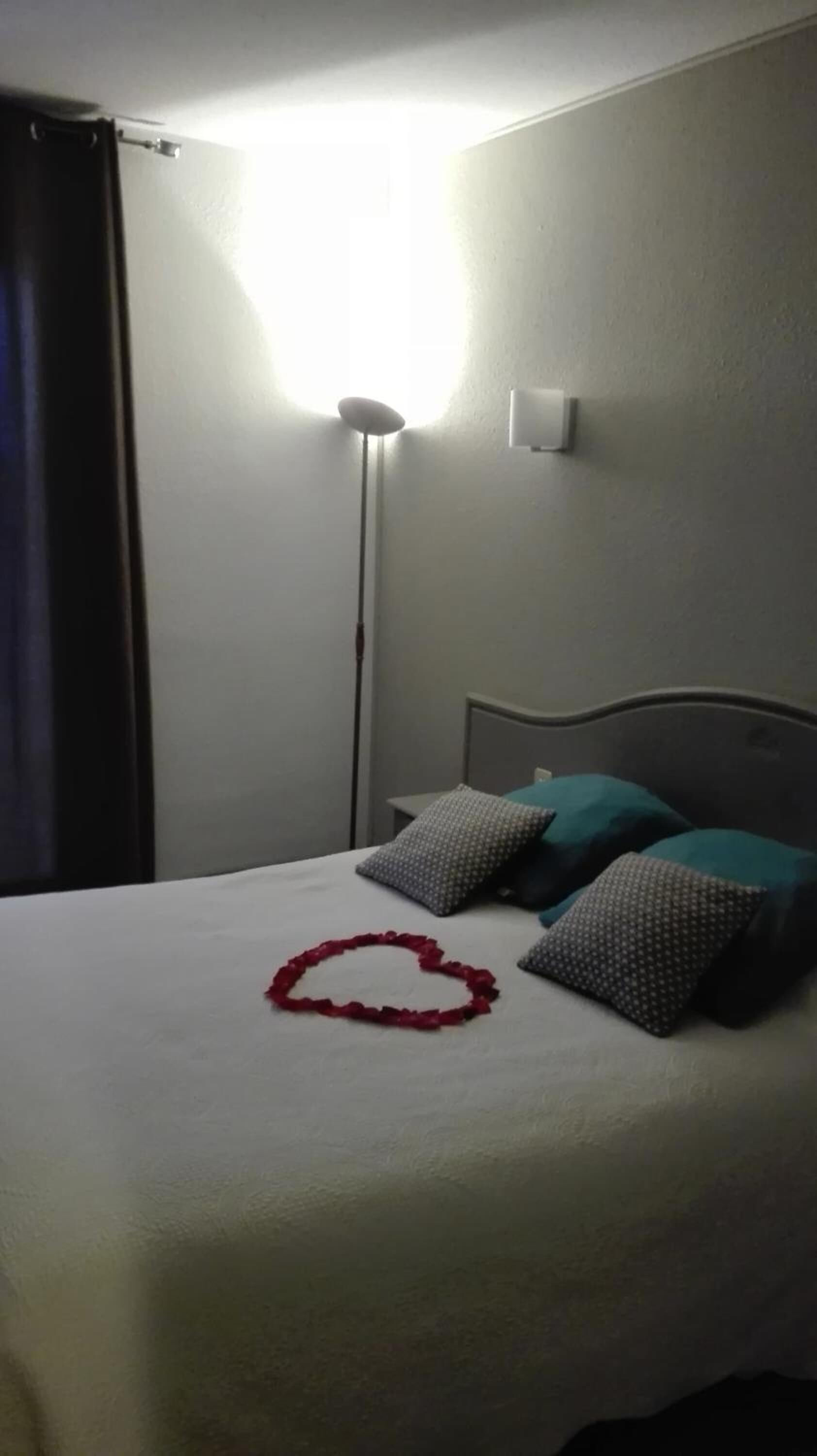 Una habitación de hotel con cama, mesita de noche, lámpara y termostato en la pared.