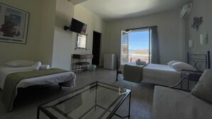 Une chambre d’hôtel avec deux lits, une table basse en verre, un bureau, une chaise et une grande fenêtre donnant sur un paysage agréable.