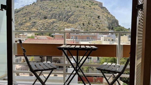 Un balcon avec deux chaises et une table, donnant sur une colline sur laquelle se trouve un bâtiment.
