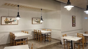 L’intérieur d’un restaurant, avec de nombreuses tables et chaises, des luminaires suspendus et des œuvres d’art accrochées aux murs.