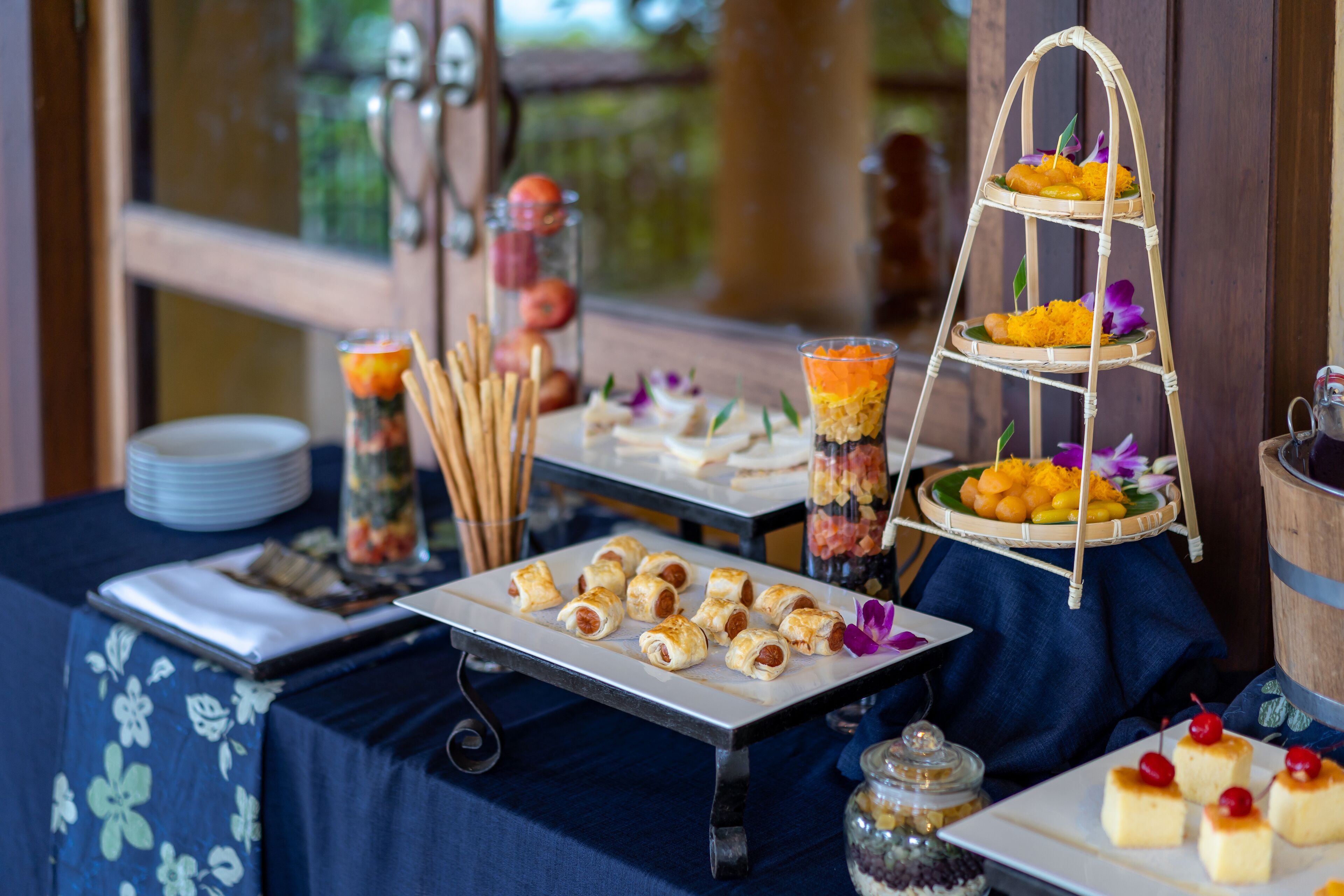 A buffet table with various food items, including a three-tiered fruit and cheese board, and a tray of mini pastries.