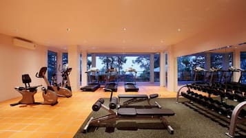 Un gimnasio con equipo de ejercicio, una banca de pesas y una hilera de mancuernas.