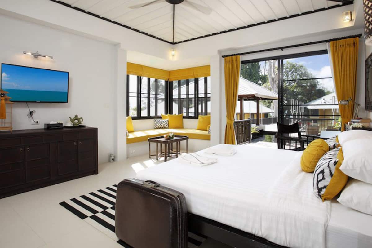 Une chambre moderne avec un grand lit, une télévision, un canapé près de la fenêtre et un balcon avec des rideaux jaunes.