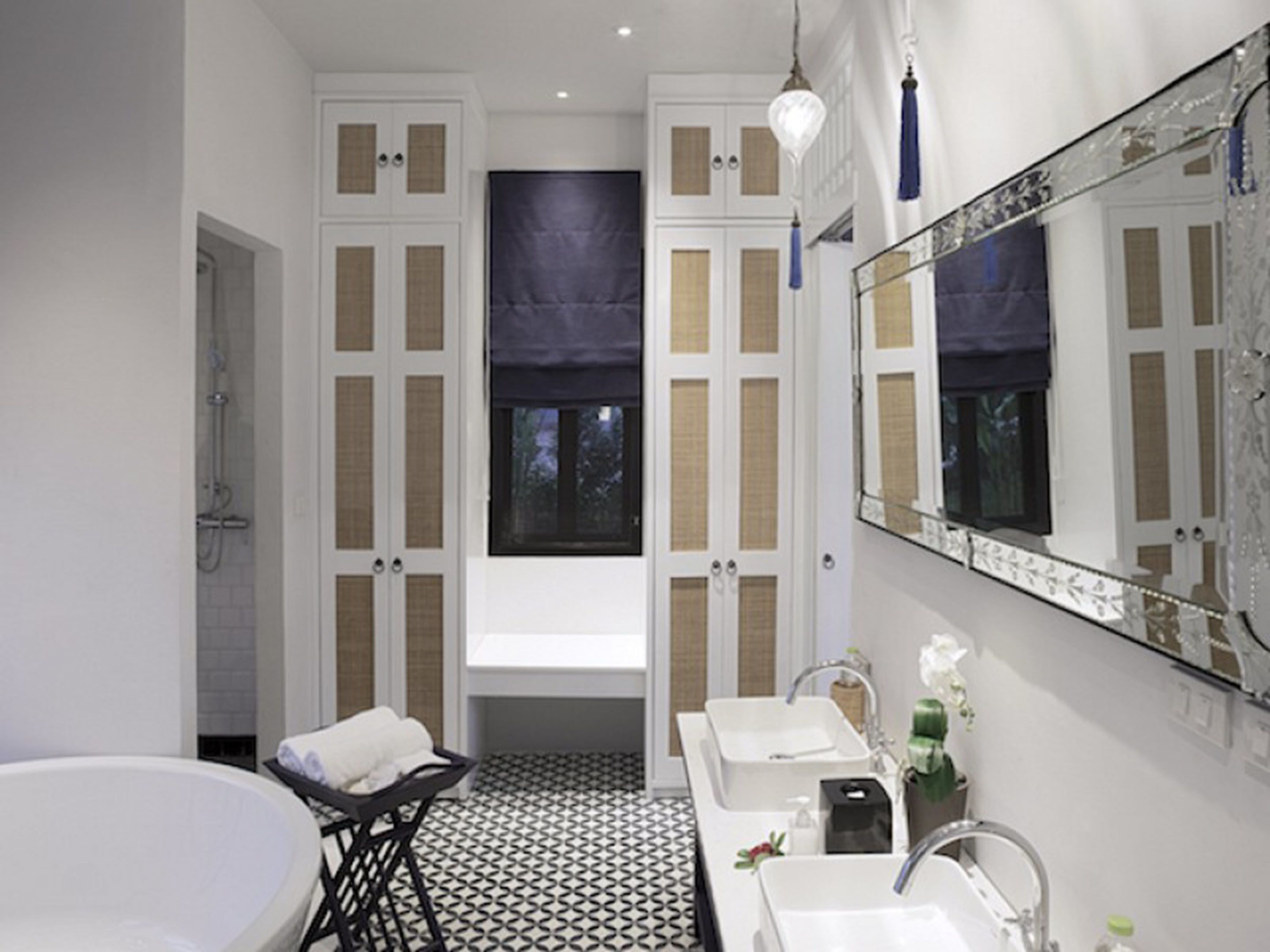 Een badkamer met een bad, twee wastafels, een grote spiegel en een raam met een donker gordijn.