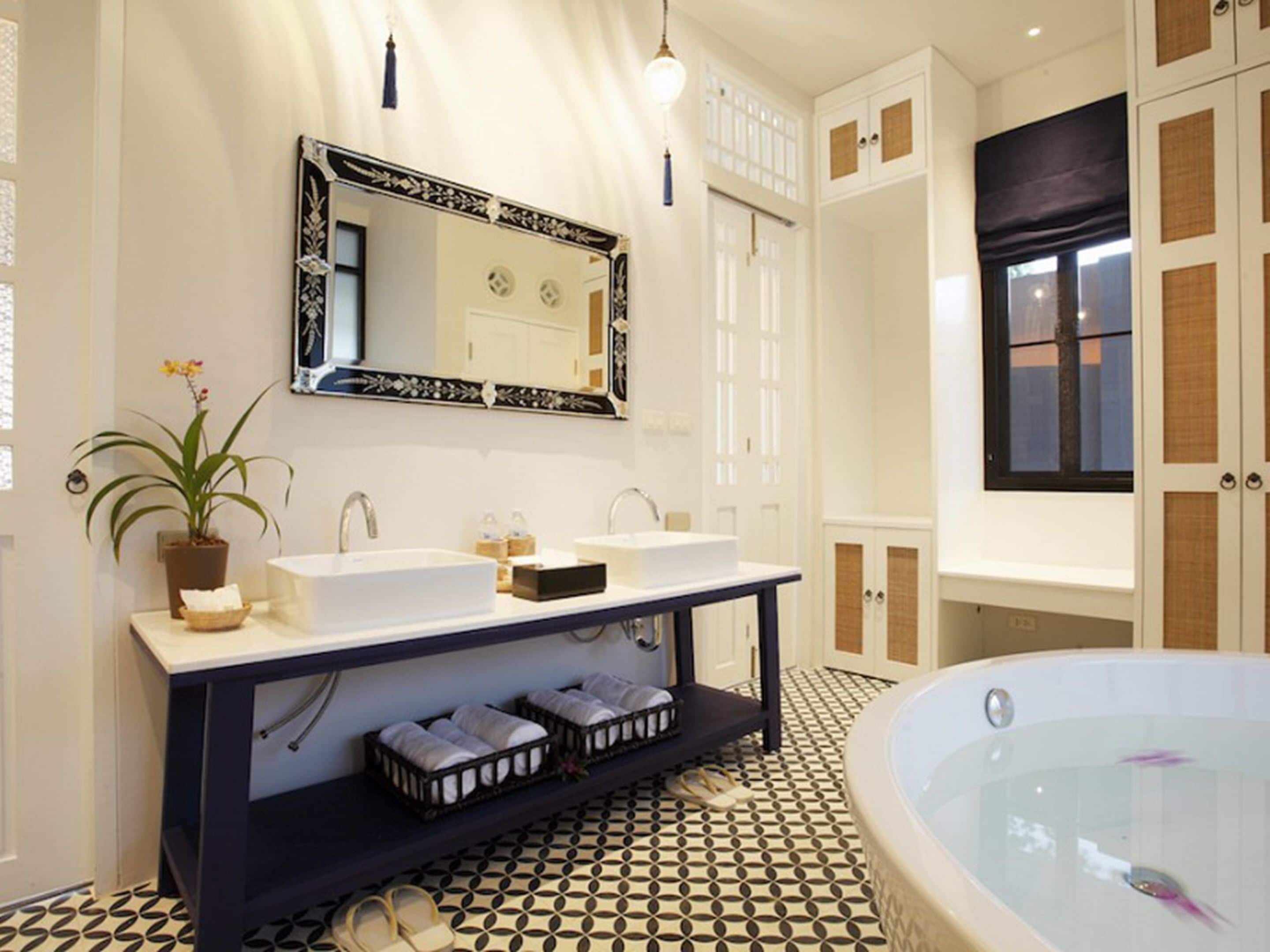 A bathroom with a large bathtub, two sinks, a mirror, and a potted plant.