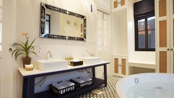 A bathroom with a large bathtub, two sinks, a mirror, and a potted plant.