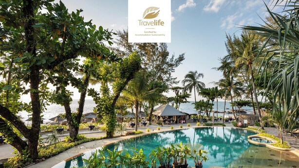 Zwembad van een resort met uitzicht op zee, omringd door palmbomen en terrasjes.