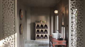 A hallway with a patterned floor, a wooden cabinet with rolled towels, a sink, and decorative panels.