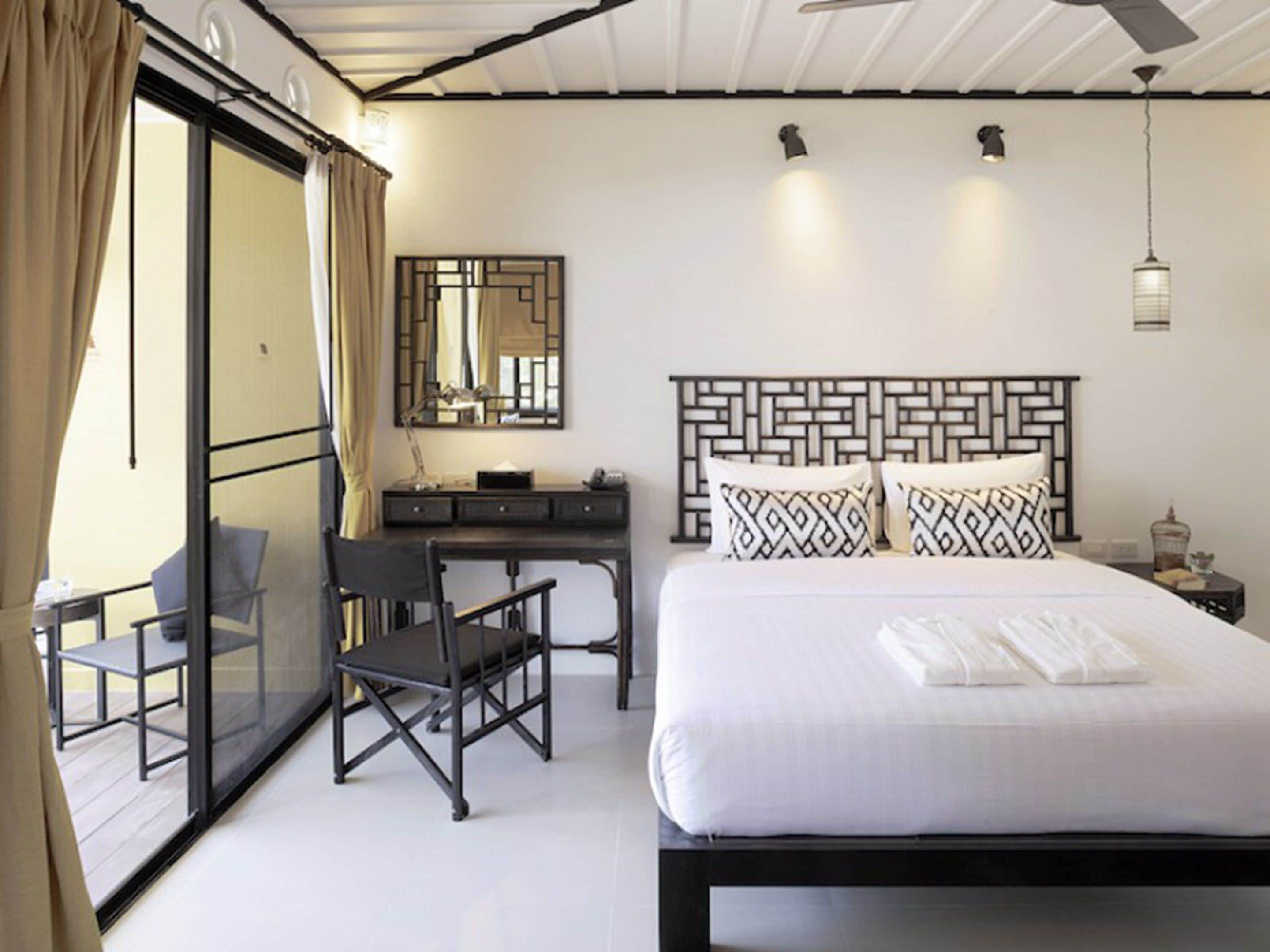 A hotel room with a bed, a desk, a chair, a mirror, and a ceiling fan.