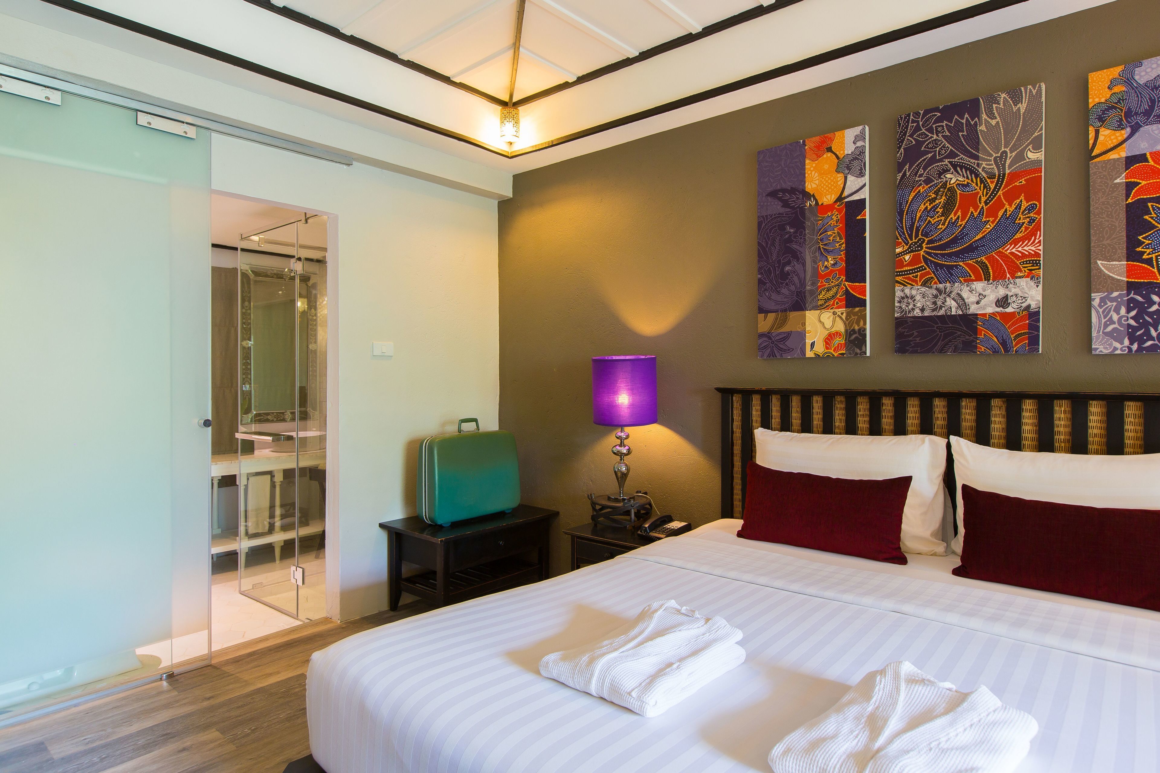 A hotel room with a bed, a nightstand, a lamp, a suitcase, and a glass shower enclosure.