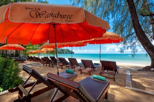 Un complejo turístico en la playa con múltiples tumbonas y sombrillas naranjas, identificado como 'Khao Lak Wanaburee Resort'.