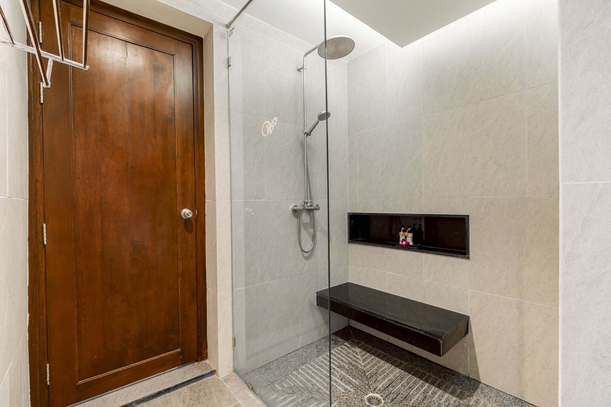 Un baño moderno con puerta de madera, cabina de ducha de vidrio y estante negro.