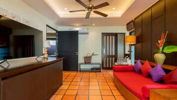 A hotel lobby with a reception desk, a red sofa with cushions, a ceiling fan, and a tiled floor.