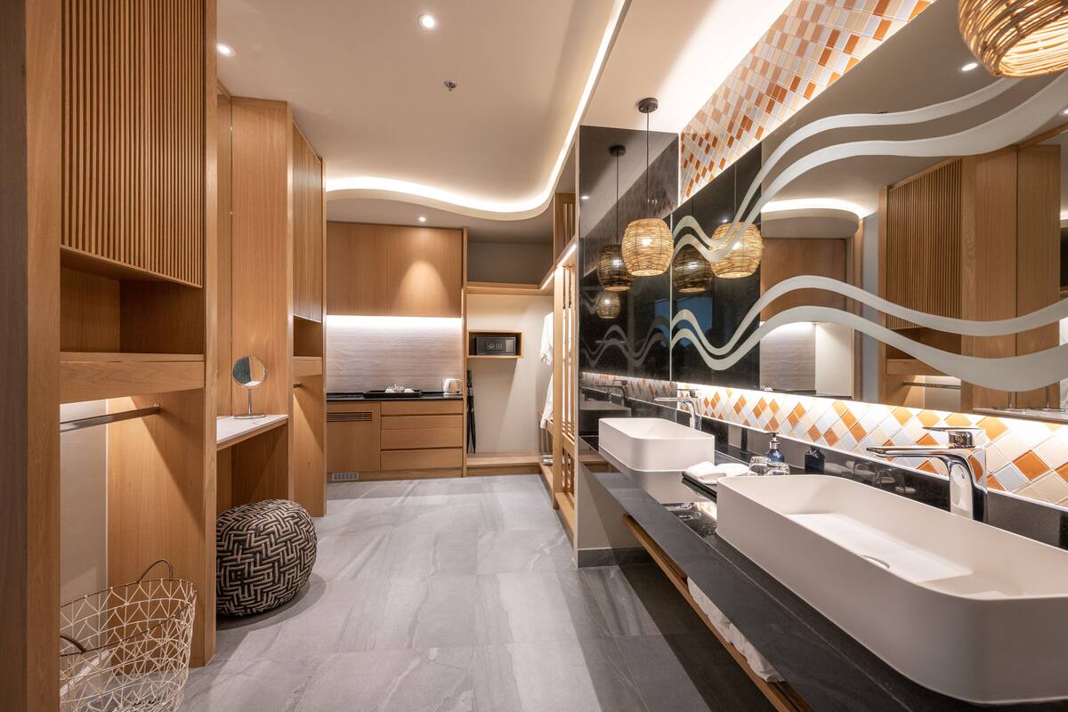 A modern bathroom with wooden cabinetry, a large mirror, two sinks, and a patterned floor.