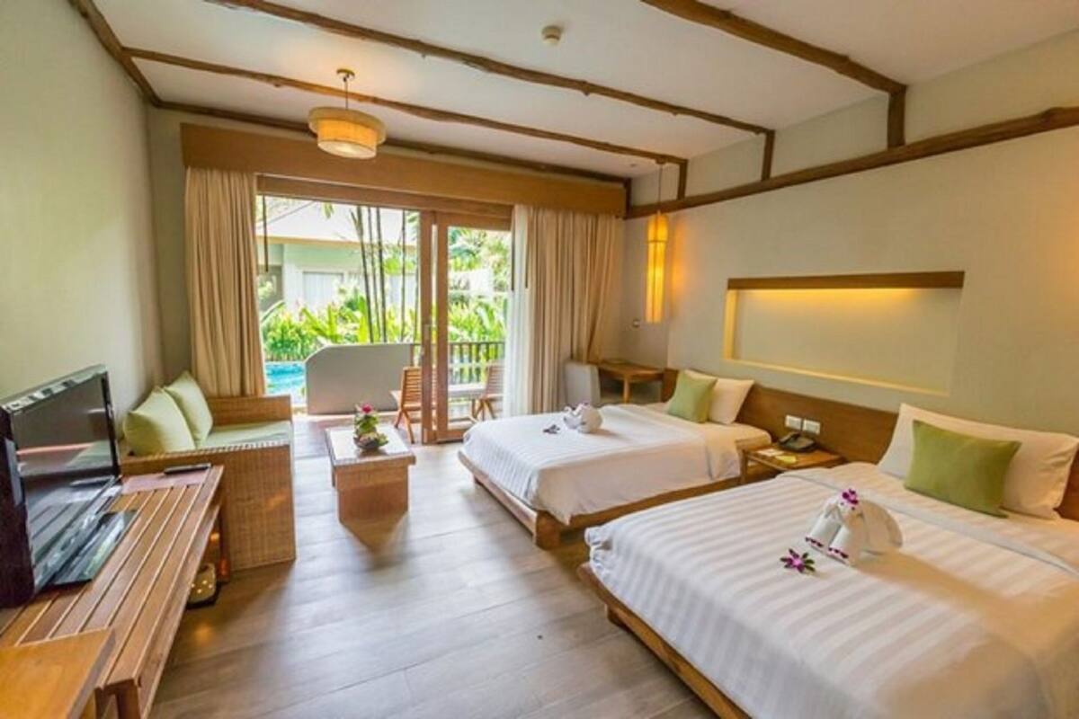 A hotel room with two beds, a TV, a desk, and a balcony with curtains.