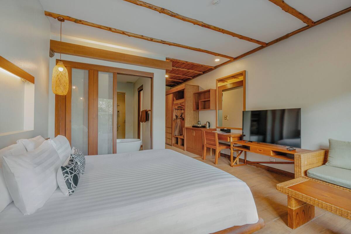 A bedroom with a bed, a desk, a TV, and a wicker chair.