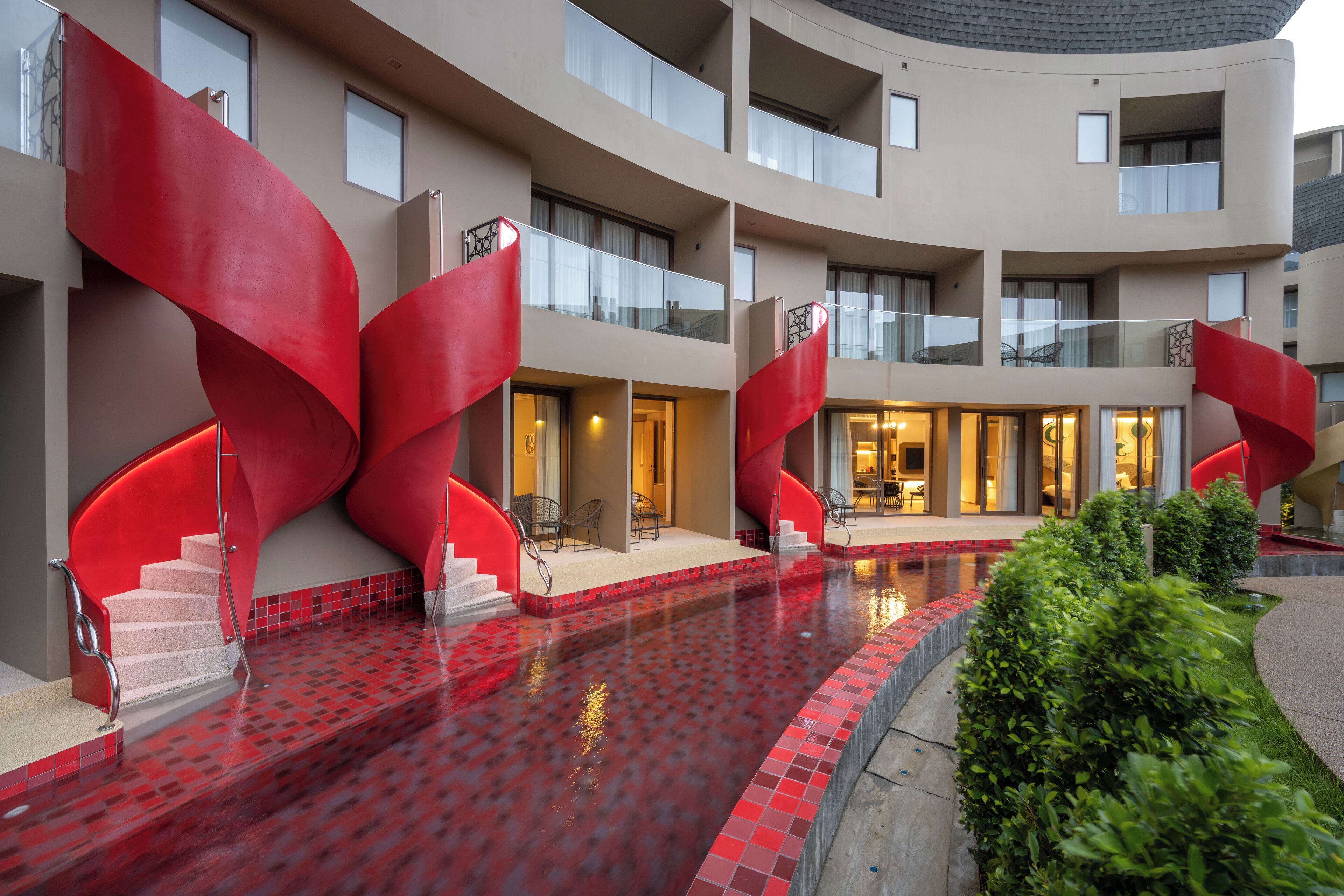 Un hôtel moderne à la façade incurvée, doté d’une cour intérieure avec une piscine aux carreaux rouges et d’espaces de détente en plein air.