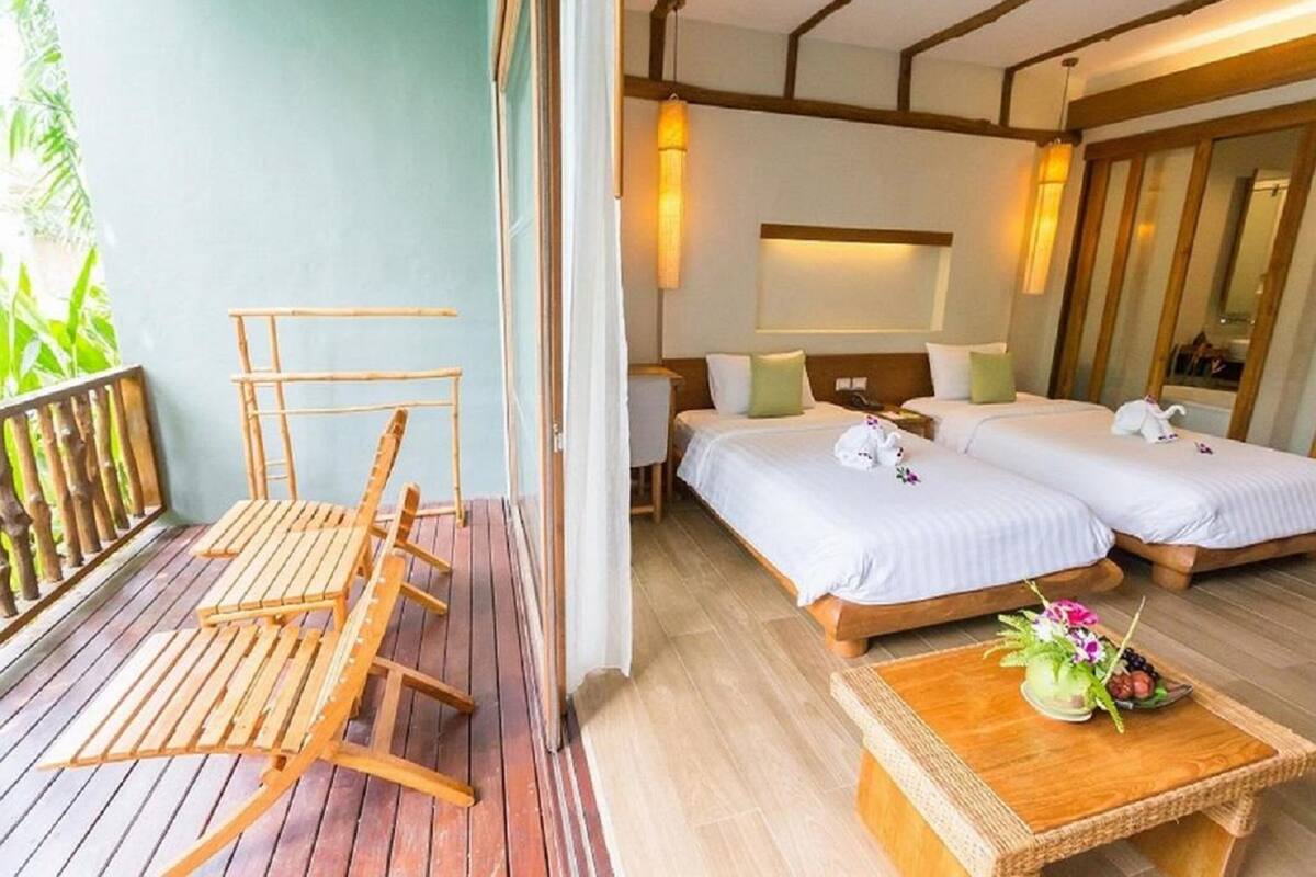 A hotel room with two beds, a wooden table with a vase of flowers, and a balcony with a wooden chair.