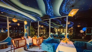 A restaurant with a modern interior, featuring blue upholstered seating, tables set for dining, and a ceiling with illuminated patterns. - Metadee Concept Hotel (Karon)