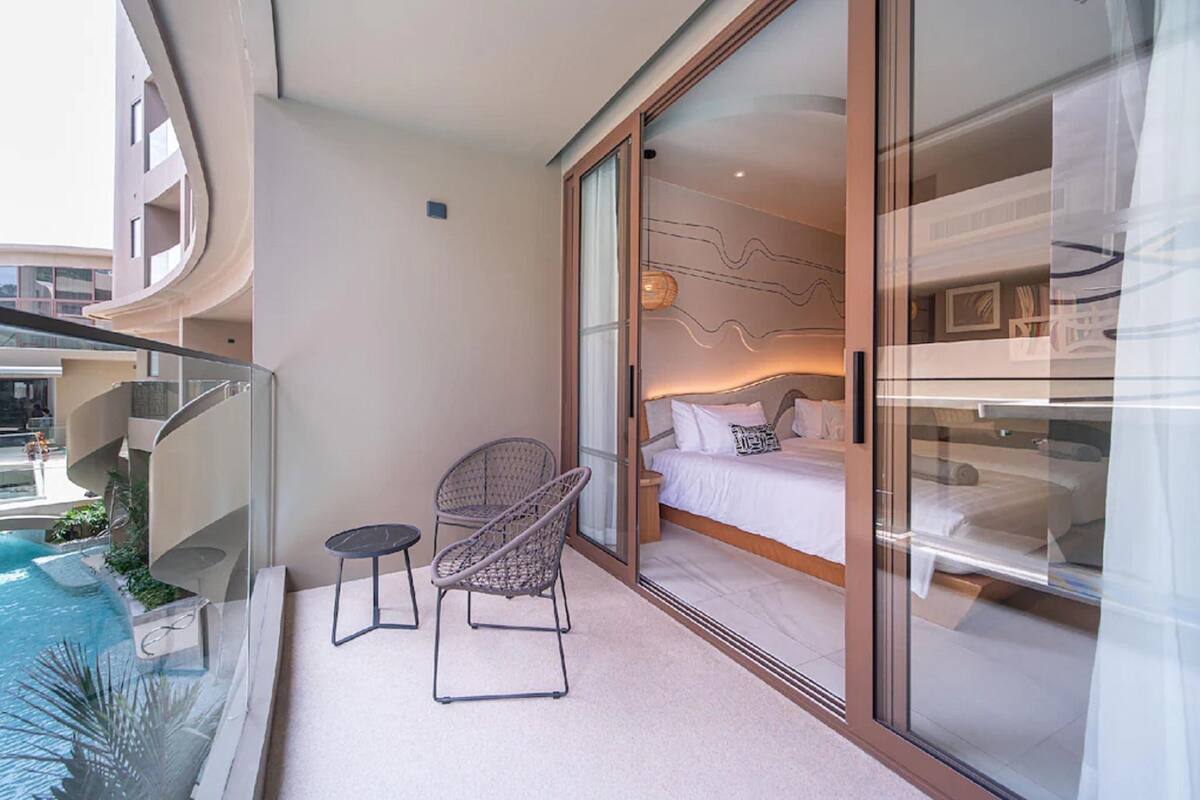 A balcony with a glass door leading to a bedroom, a small table, and a wicker chair.