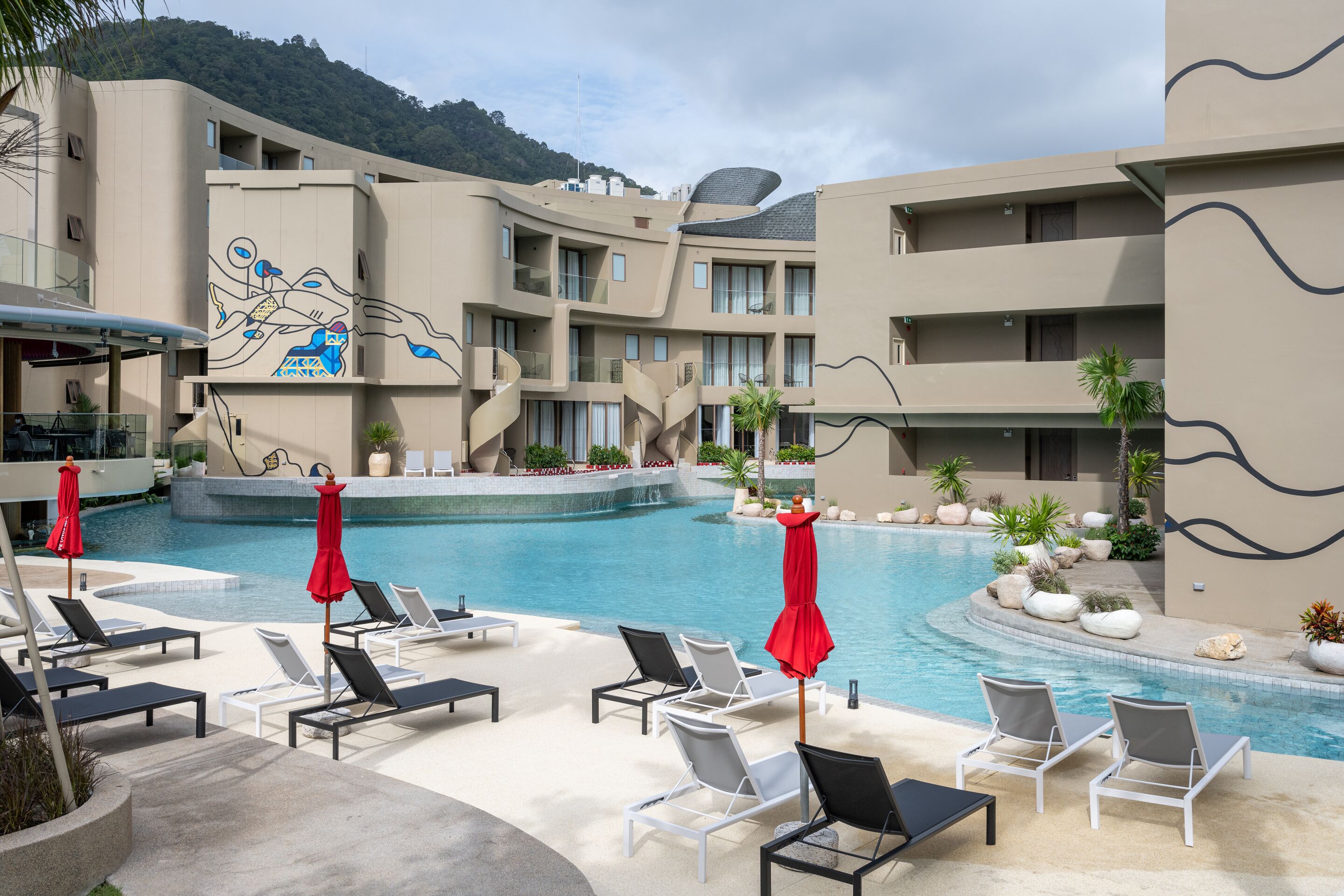Un hôtel doté d’une piscine, de chaises longues et de parasols rouges.