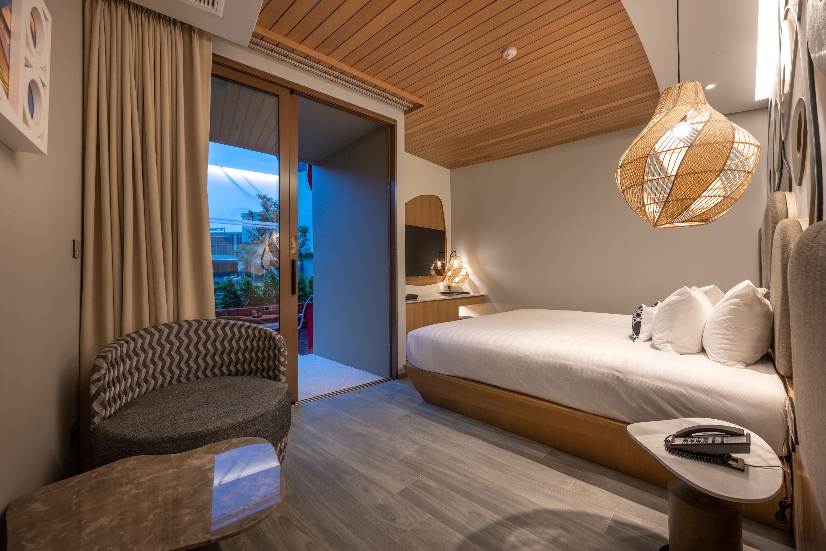 Una habitación de hotel moderna con una cama grande, un sofá, una pequeña mesa y una lámpara colgante.
