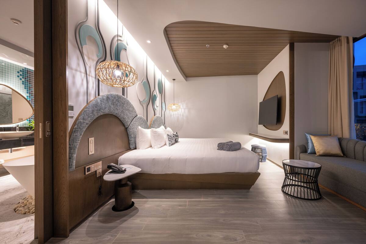 A modern bedroom with a large bed, bedside tables, a TV, and a view of the city.