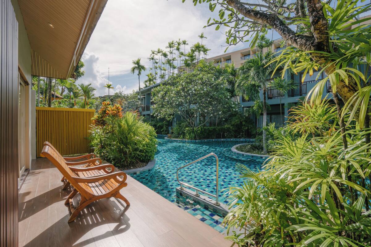 A pool area with lounge chairs, a pool with a tiled pattern, and surrounding tropical plants.