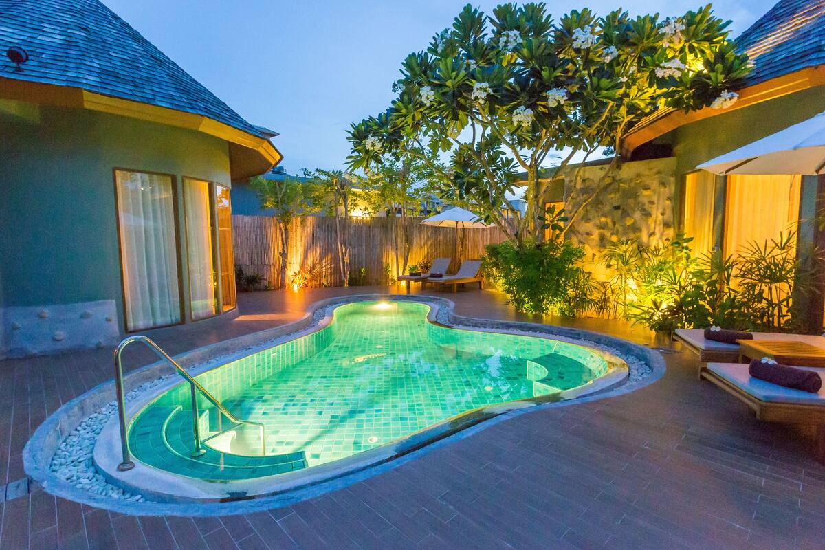 A swimming pool with a curved edge, surrounded by lounge chairs and a wooden fence.