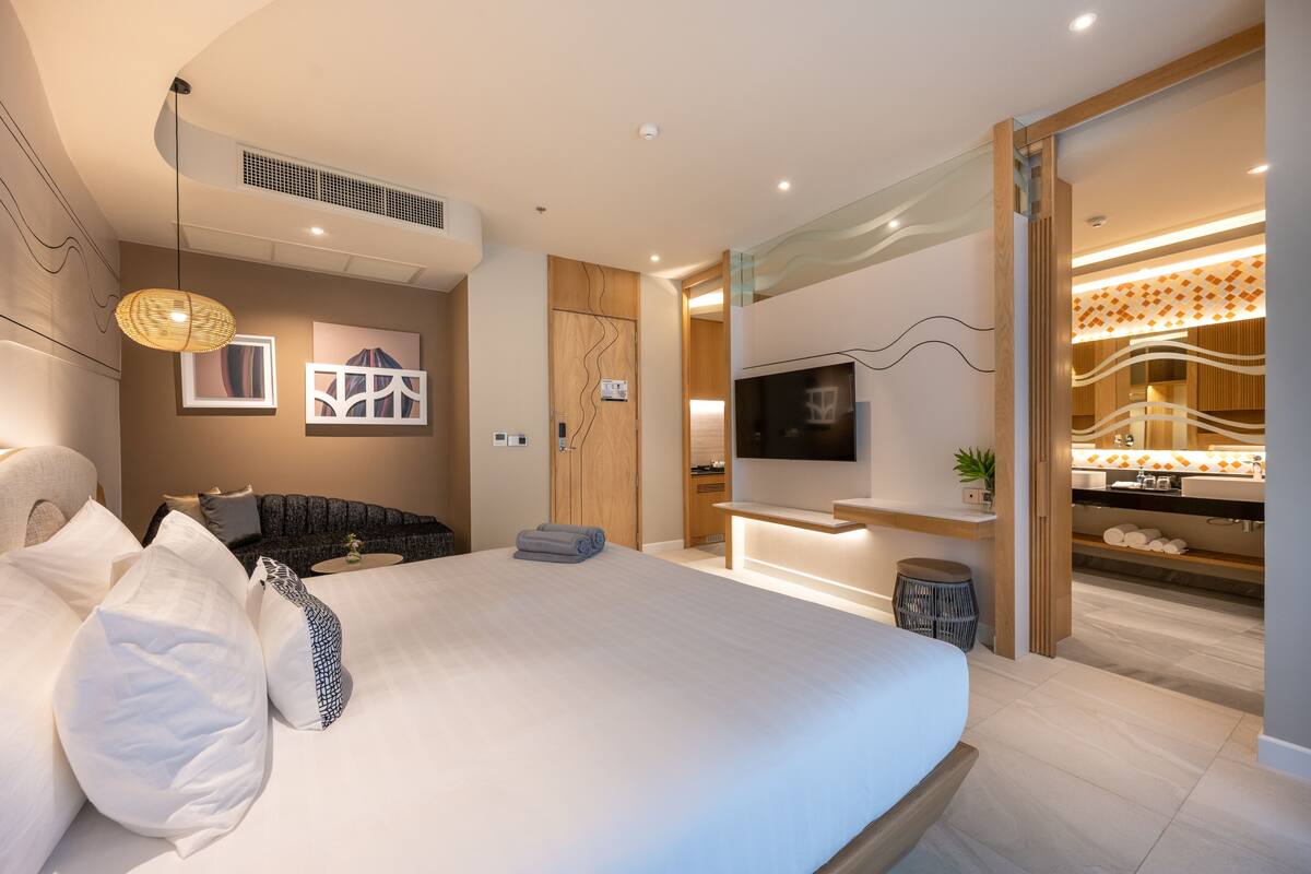 A modern hotel room with a large bed, a TV mounted on the wall, and a bathroom with a vanity and sink.