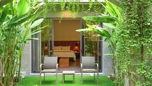 Una habitación de hotel moderna con una puerta de vidrio, una cama, dos sillas y una mesita.