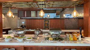 Montaje de bufé con diferentes platillos y un chef al fondo.