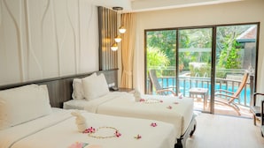 A hotel room with two beds, a balcony with a pool, and a view of greenery. - Nipa Resort (Patong)