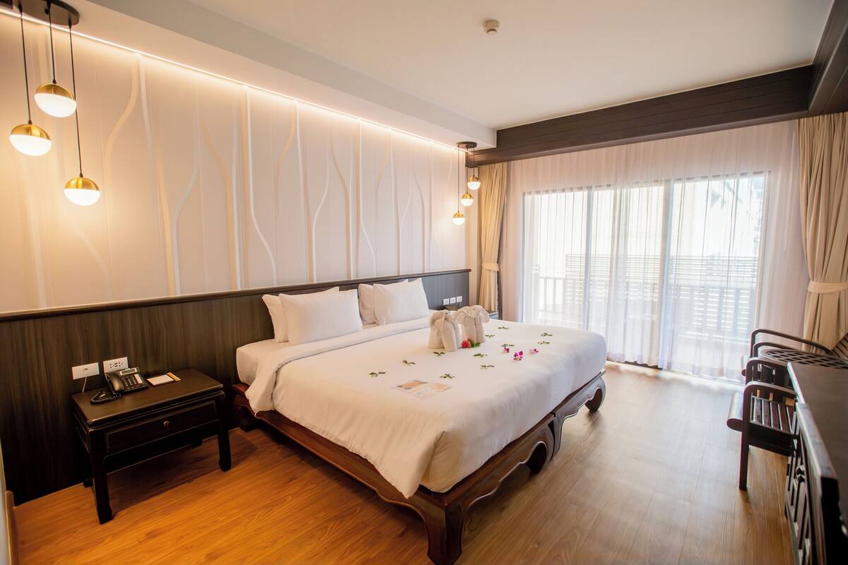 Quarto de hotel com uma cama grande, mesas de cabeceira, escrivaninha e uma janela com cortinas.