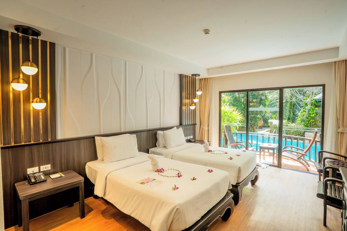 Quarto de hotel com duas camas, uma secretária pequena, telefone e vista para uma piscina e vegetação.