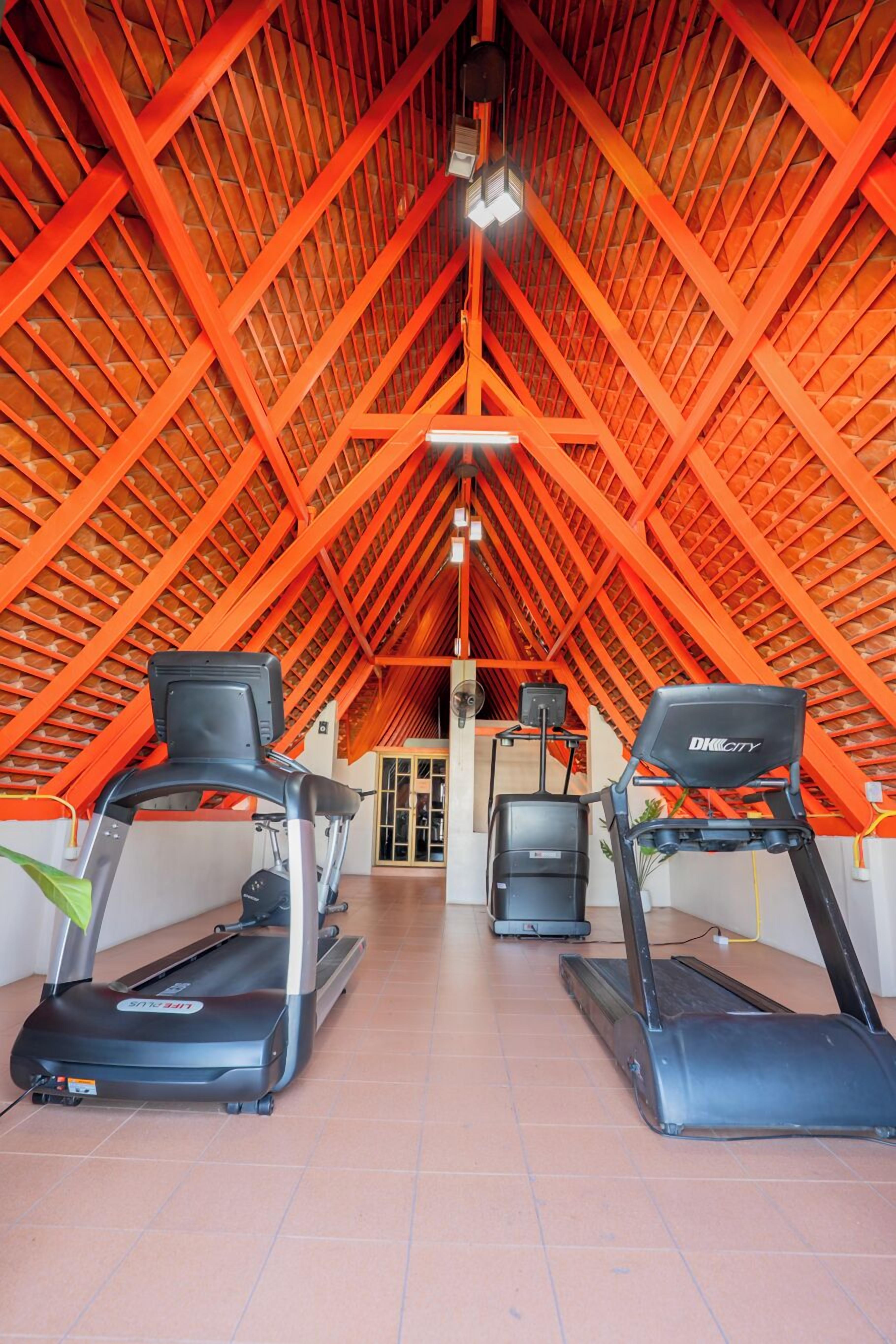An indoor gym with two treadmills, a ceiling with a red truss structure, and a door leading to another room.