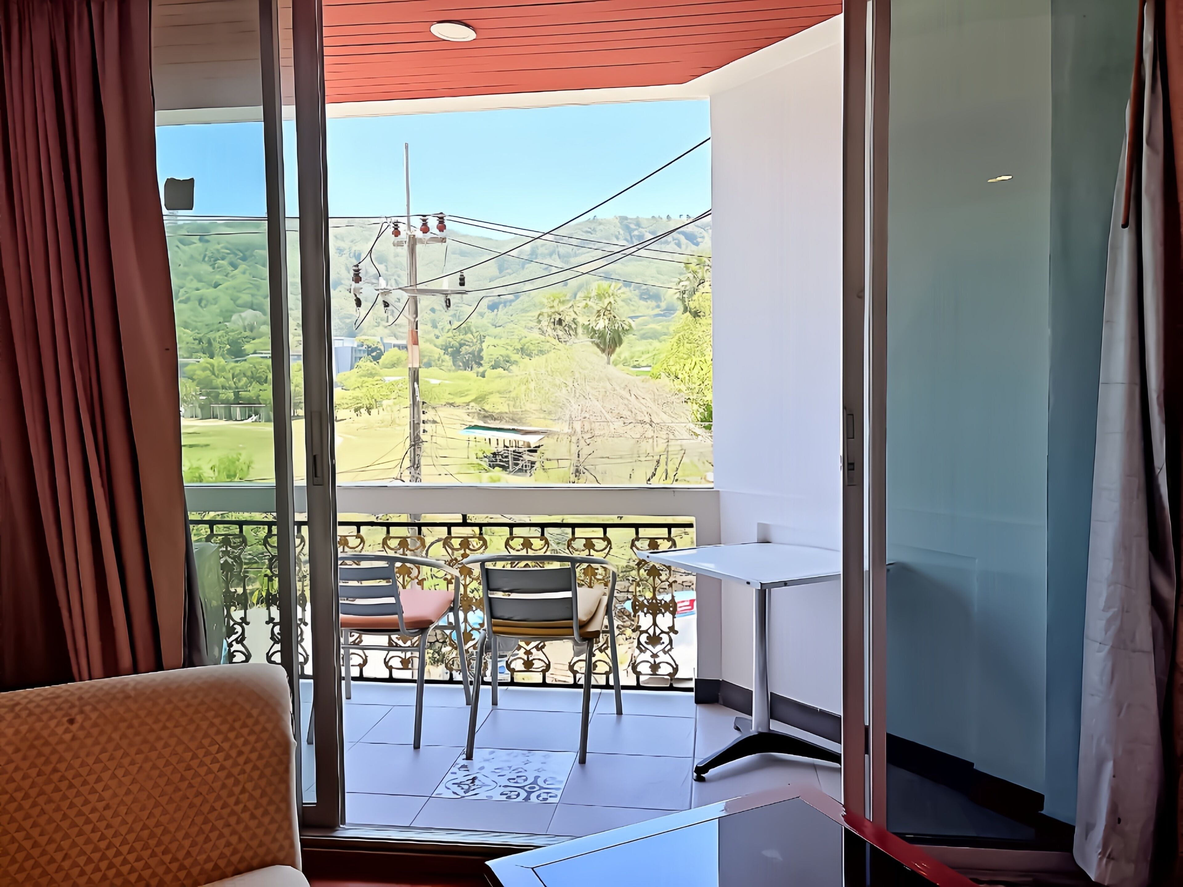A balcony with a table and chairs, a view of greenery and hills, and a clear sky.