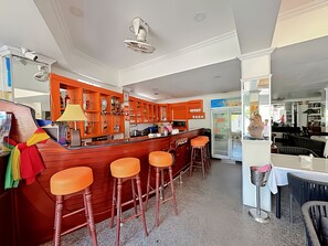 A bar area with orange stools, a refrigerator, and a dining area with a table and chairs. - Orchid Hotel and Spa Kalim Bay (Patong)