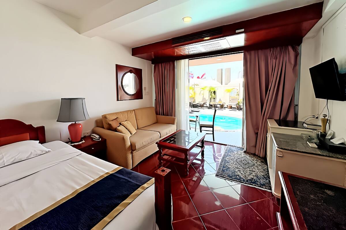 Ein Hotelzimmer mit Bett, Sofa, Schreibtisch, Fernseher und Blick auf den Poolbereich.