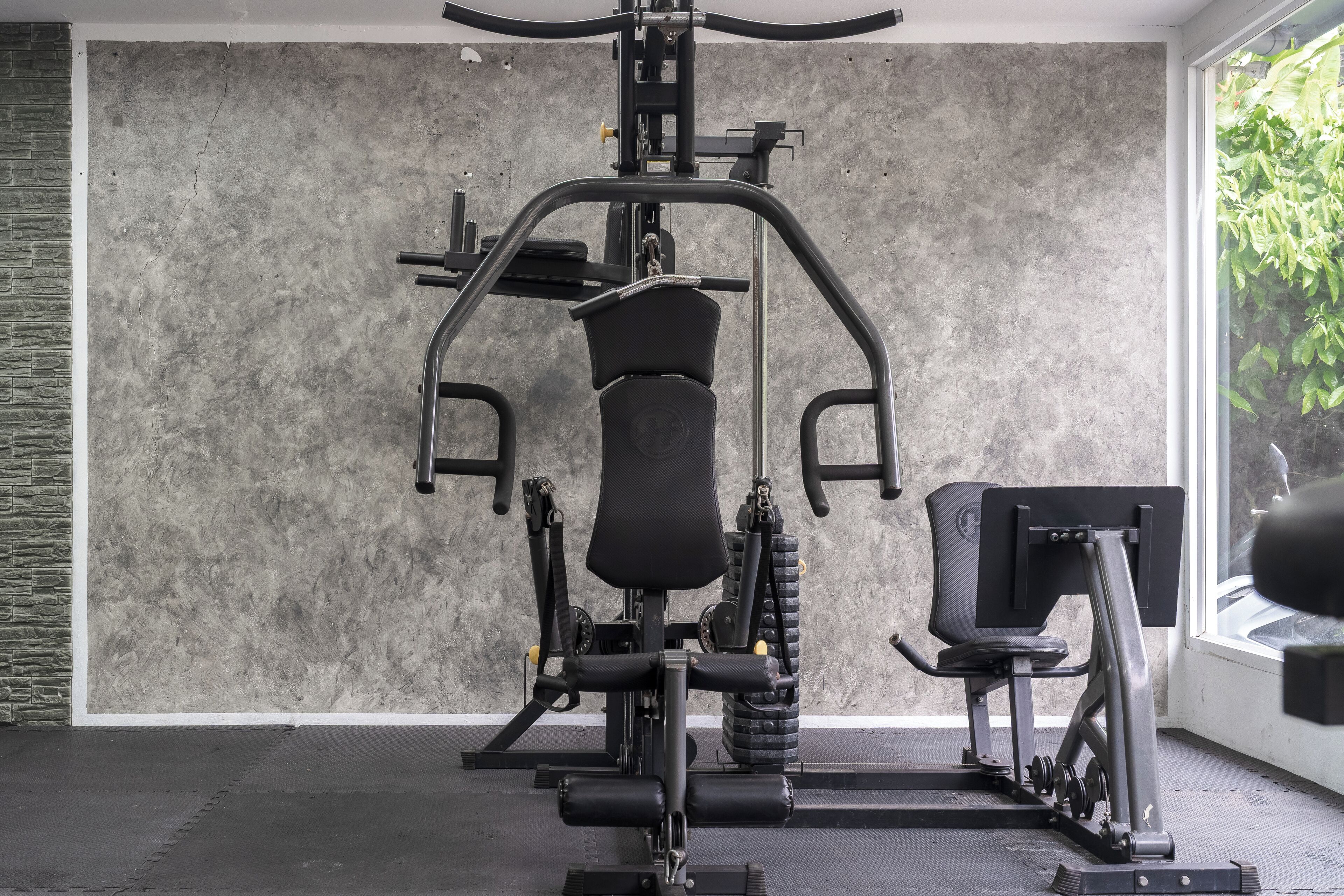 Une salle de sport équipée d’une machine de musculation, d’un banc et d’un support mural pour les poids.